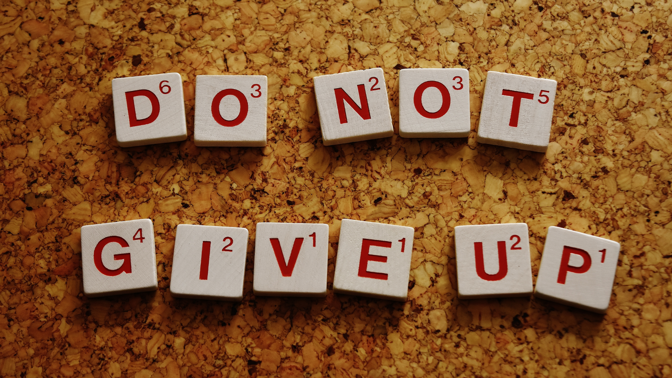 Scrabble letters on a cork board that spell out the words "do not give up".