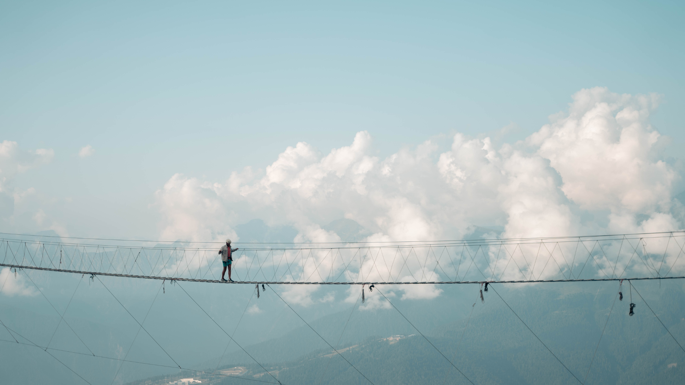Person walking across a thin wire bridge, high up in the mountains