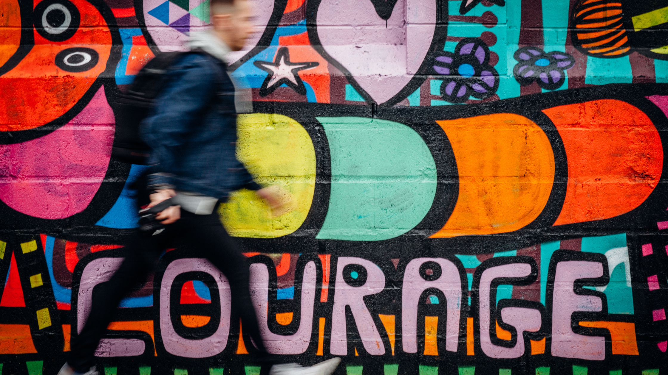 Man walking past a colourful mural that says "courage"