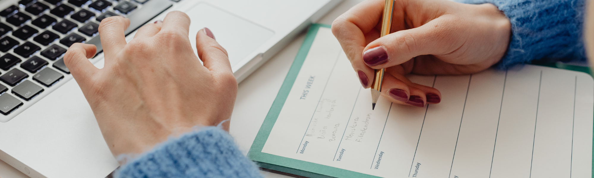 Image shows the arms of a lady wearing a light blue sweater, writing down her goals for the day.  Image courtesy of Canva