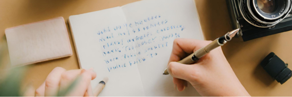 Making Freelance Writing Your Business - picture shows a woman's hand holding a pen and writing in a notebook