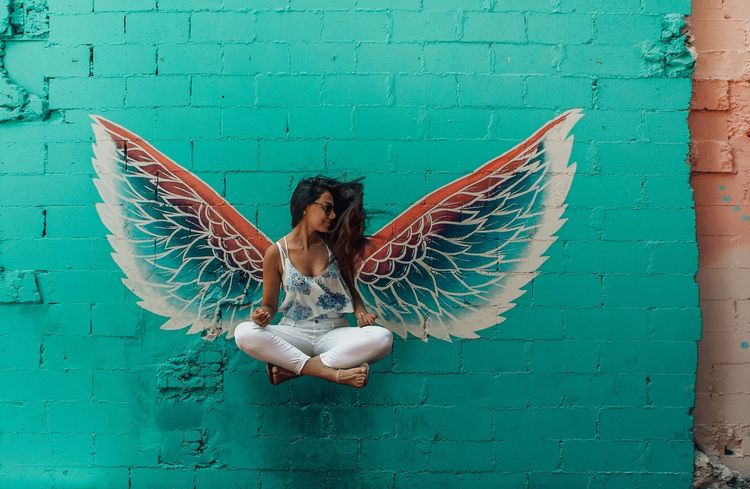 Girl wearing wings sitting against turquoise wall