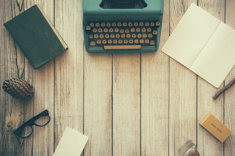 Typewriter, writing pad and reading glasses on wooden table