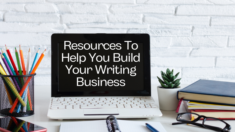Desk with coloured pencils, books, notebook, glasses and a laptop that says "resources to help you build your writing busines